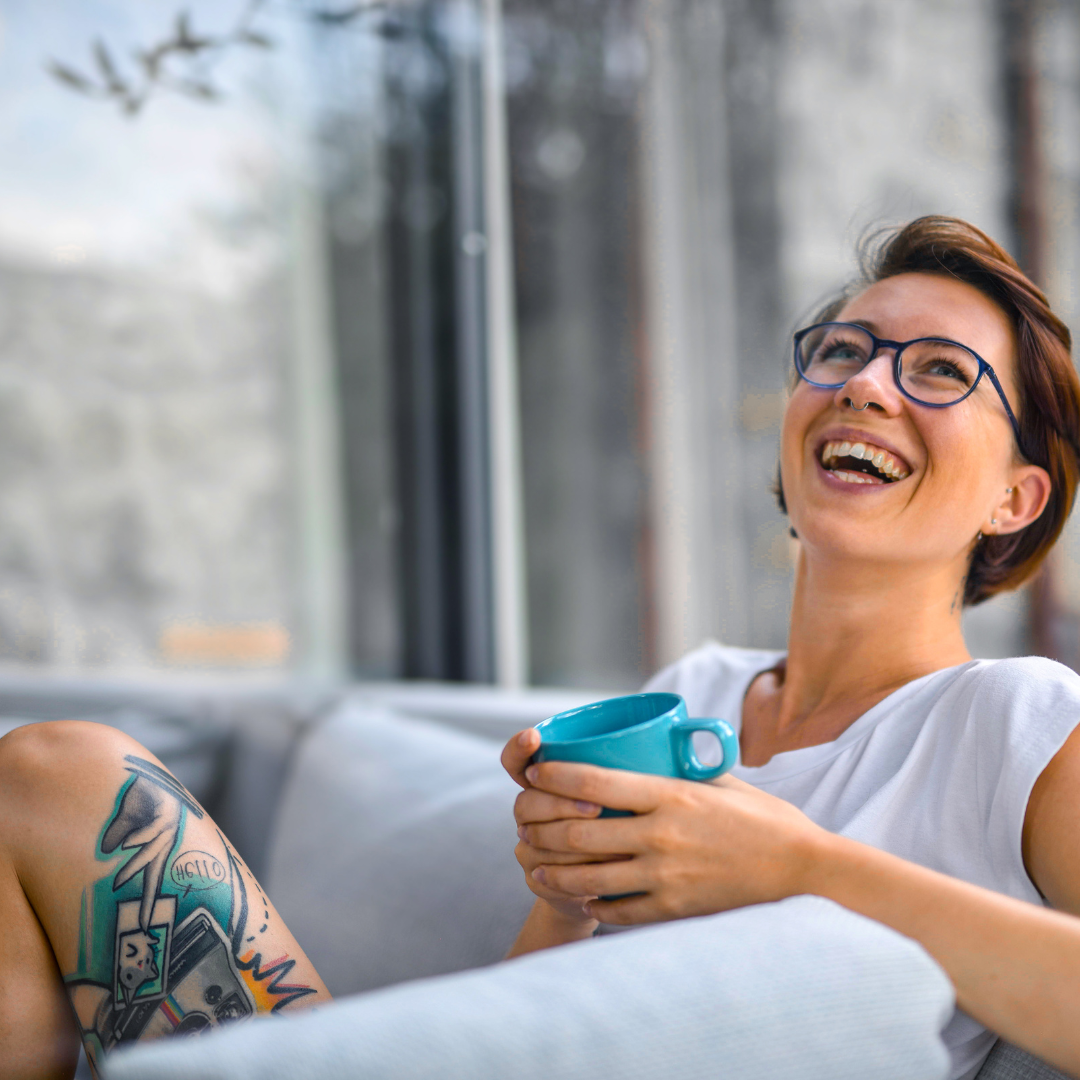Person laughing while holding a mug by a window